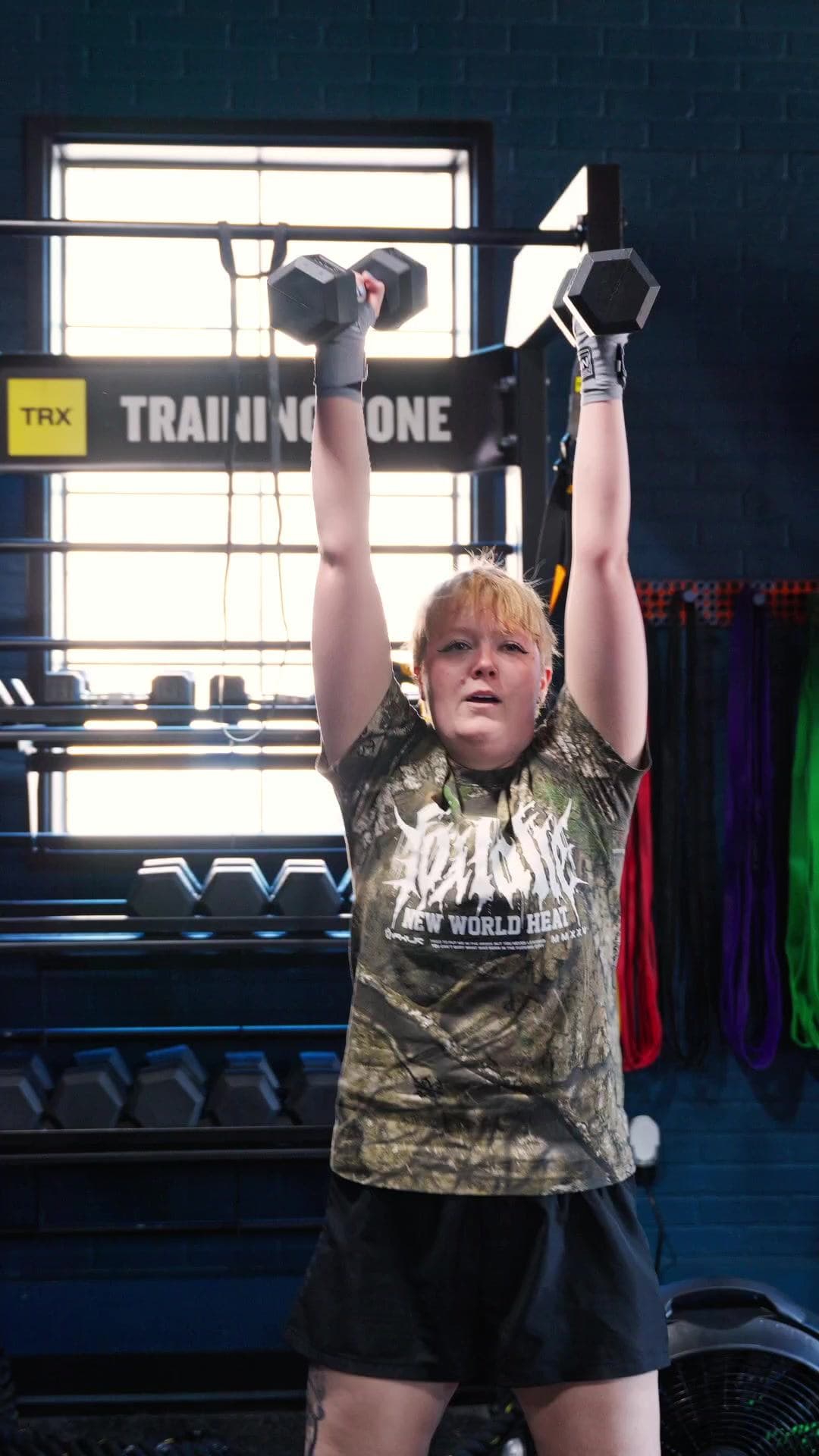 Vibes Lifestyle member pressing dumbbells overhead in the strength zone